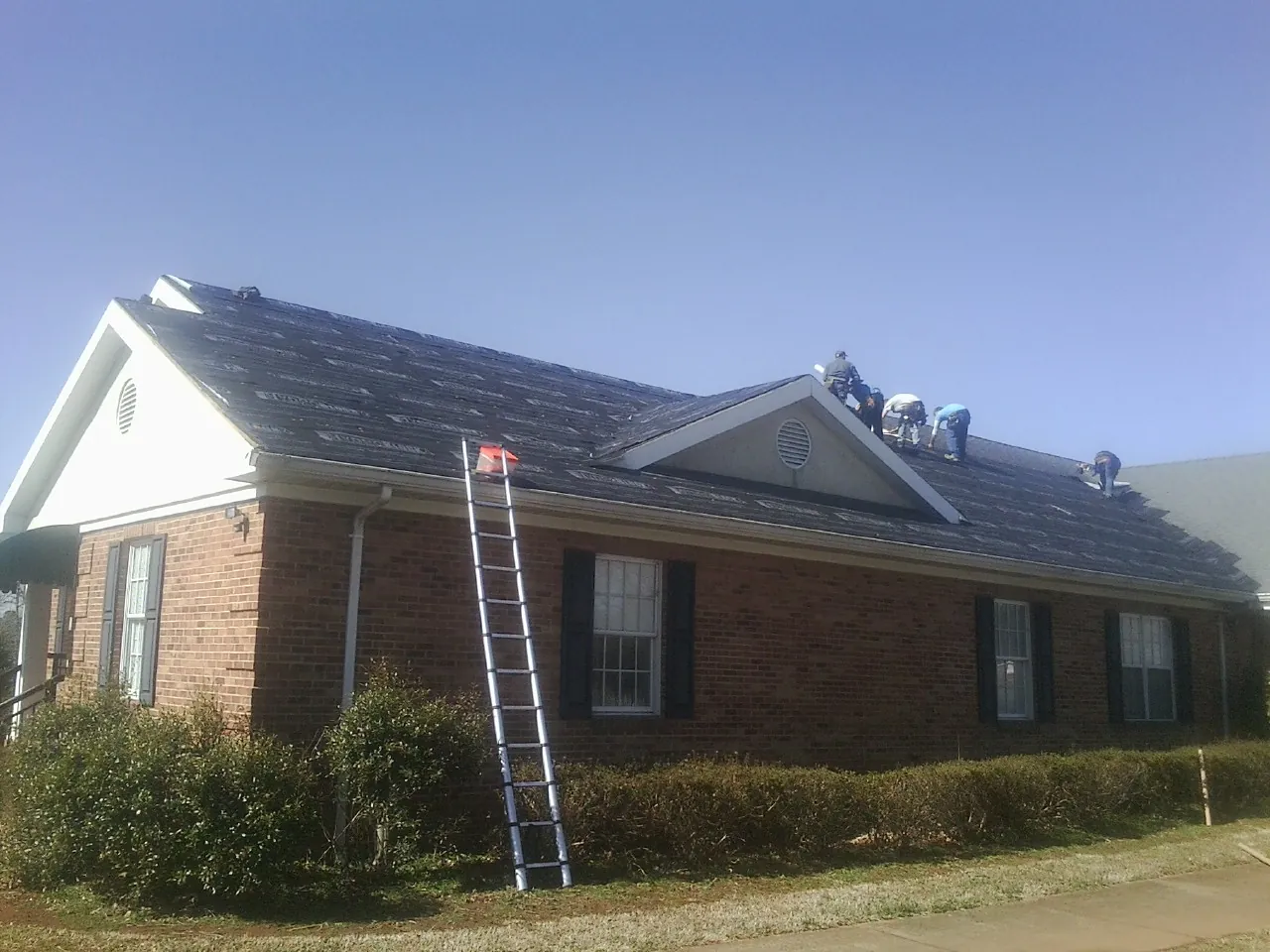 Crew tearing shingles off a brick ranch roof with a ladder set — Emergency Roof Repair work by our crew in Kingston Mines