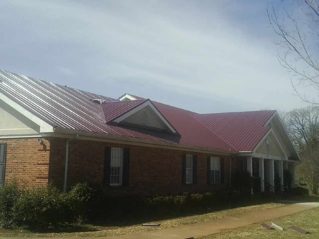 Red metal roof with gabled entries on a long brick building, from a Hail Damage Roof Repair job in Kingston Mines