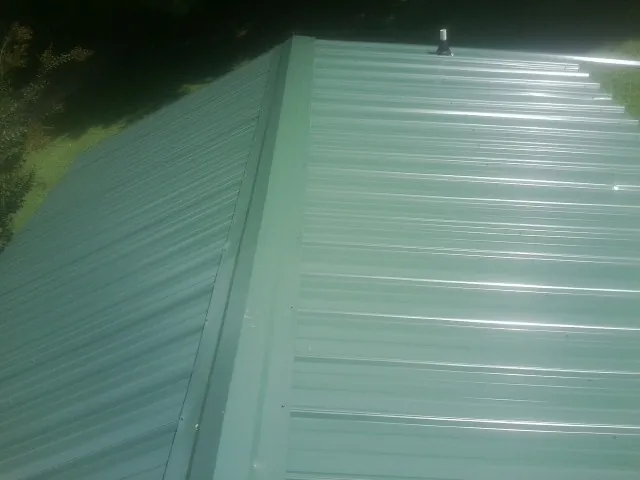 New green metal panels meeting at the ridge of a roof — Flat Roof Repair work by our crew in Kingston Mines