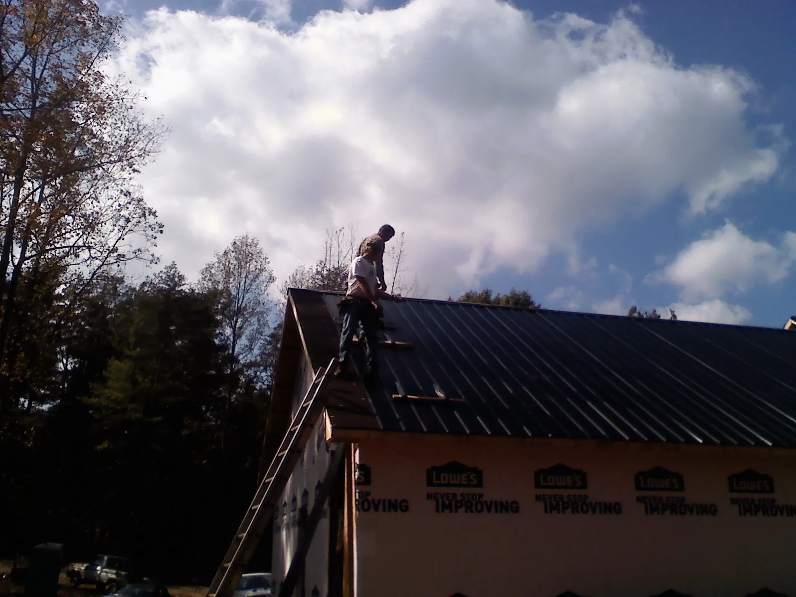 Roofer fastening dark metal panels high against a cloudy sky, from a Roof Inspection job in Kingston Mines
