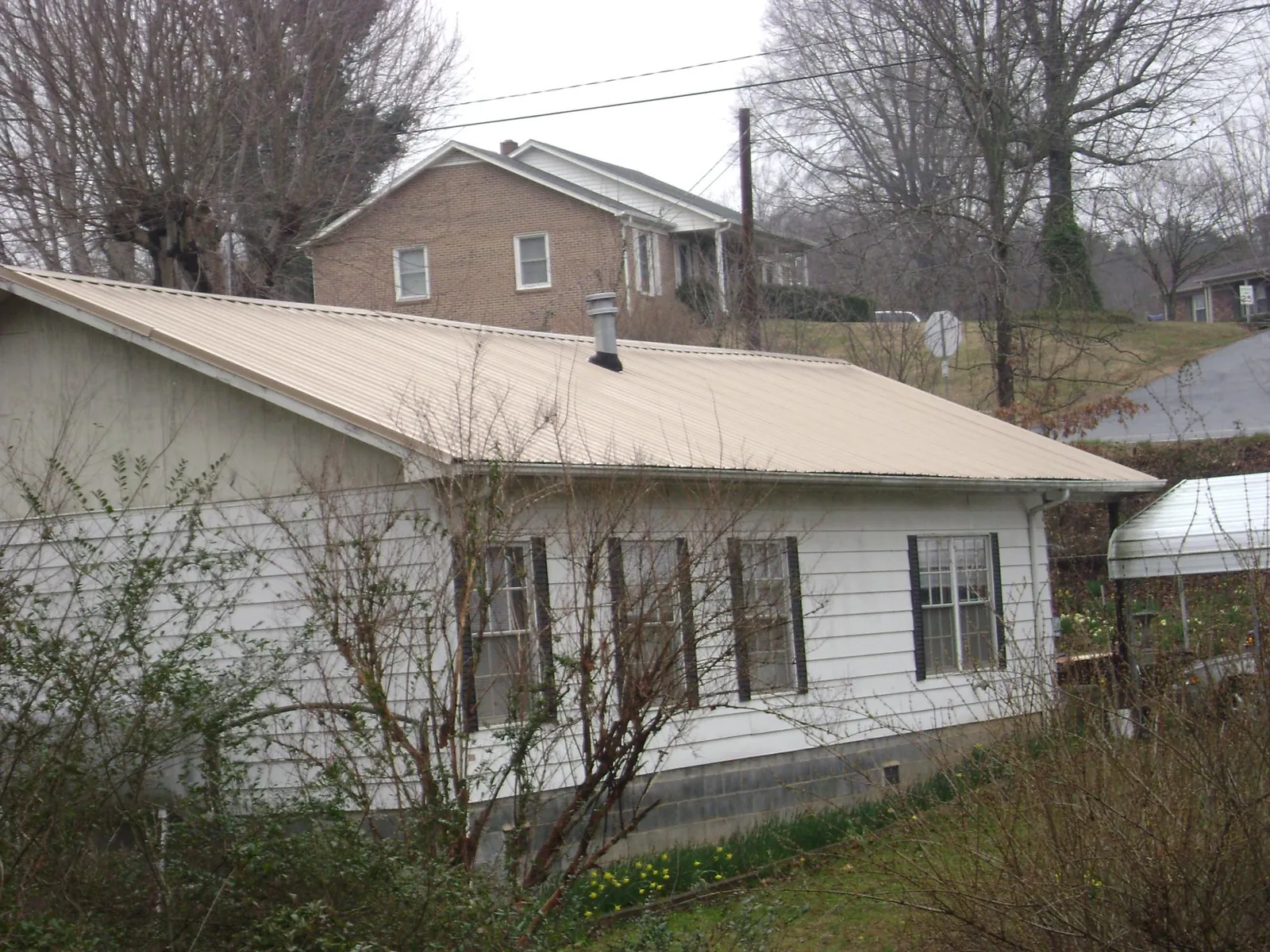 Tan metal roof on a white sided house set into a hillside — Commercial Roofing by Roofing Brothers in Kingston Mines