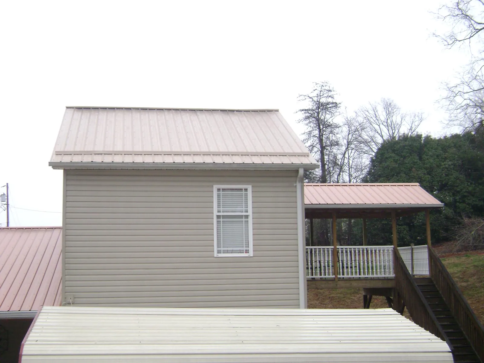 Tan metal roofs on a two story addition and attached porch, from a Roof Replacement job in Kingston Mines